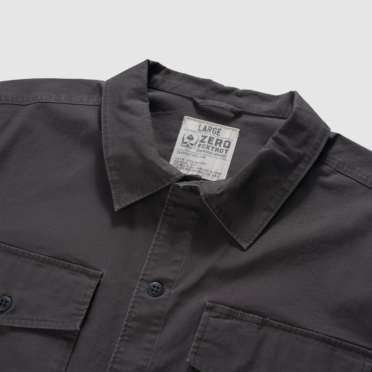 Close-up of a charcoal CPO Shirt showing the collar, button-front closure, and two chest pockets with buttons on a soft textured fabric.