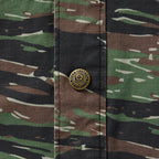 Close-up of a camouflage patterned fabric with a brass snap button featuring a skull and the text "Zero Foxtrot" on the Chore Jacket.