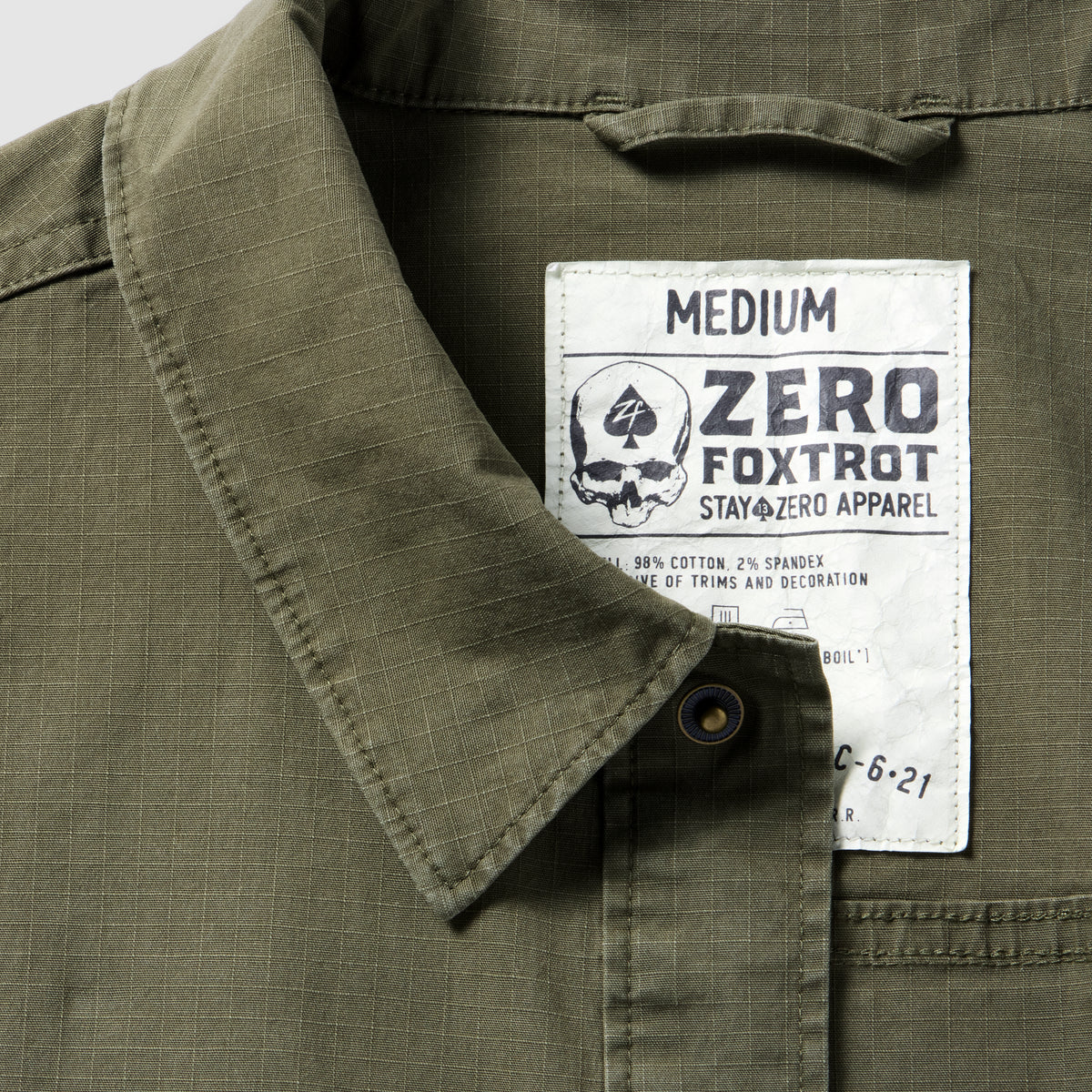 Close-up of a dark olive Chore Jacket collar and label showing medium size, made from cotton blend fabric with durable stitching details.
