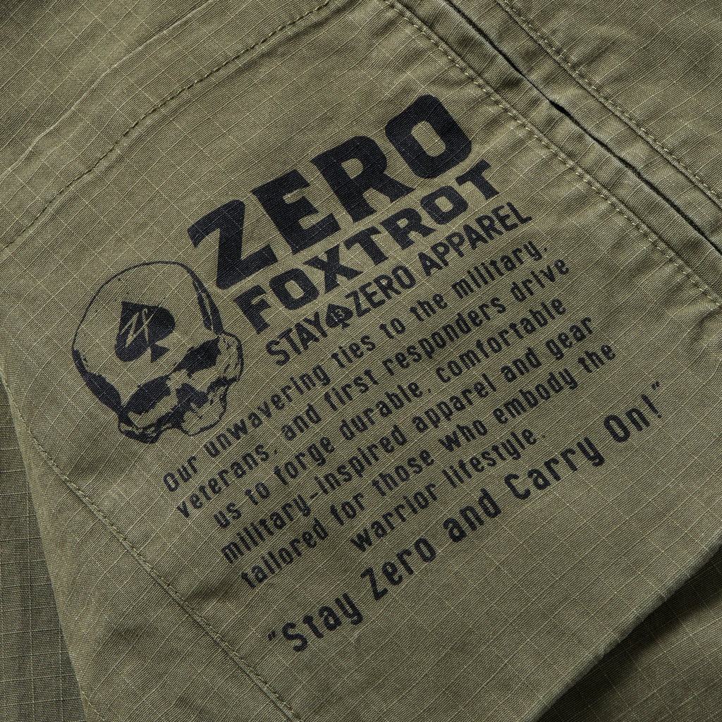 Close-up of a dark olive Chore Jacket pocket featuring a black printed military-inspired graphic with a skull, text about durable apparel for veterans and first responders, and the phrase "Stay Zero and Carry On".