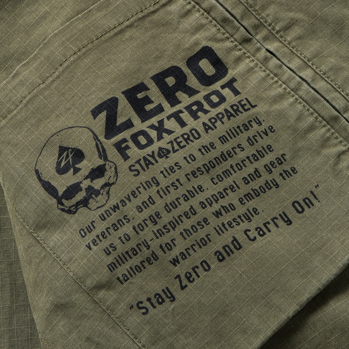 Close-up of a dark olive Chore Jacket pocket featuring a black printed military-inspired graphic with a skull, text about durable apparel for veterans and first responders, and the phrase "Stay Zero and Carry On".