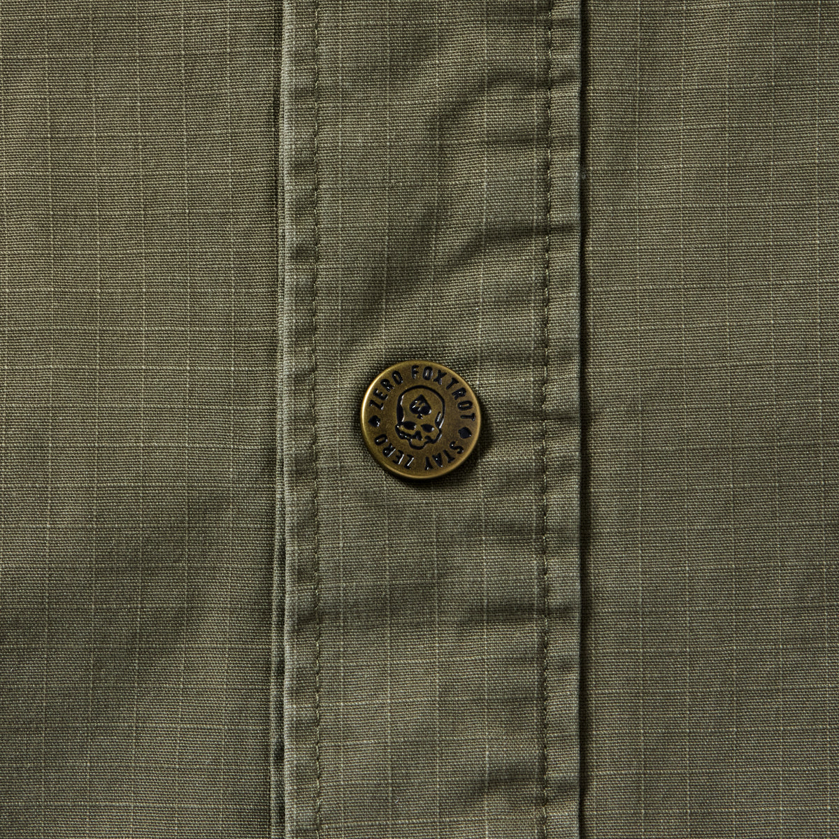 Close-up of a dark olive Chore Jacket showing textured fabric with grid pattern and a detailed metal button featuring engraved text and a skull design.