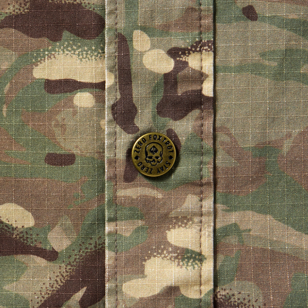 Close-up of camouflage fabric with a metal button featuring a skull design on the Chore Jacket.