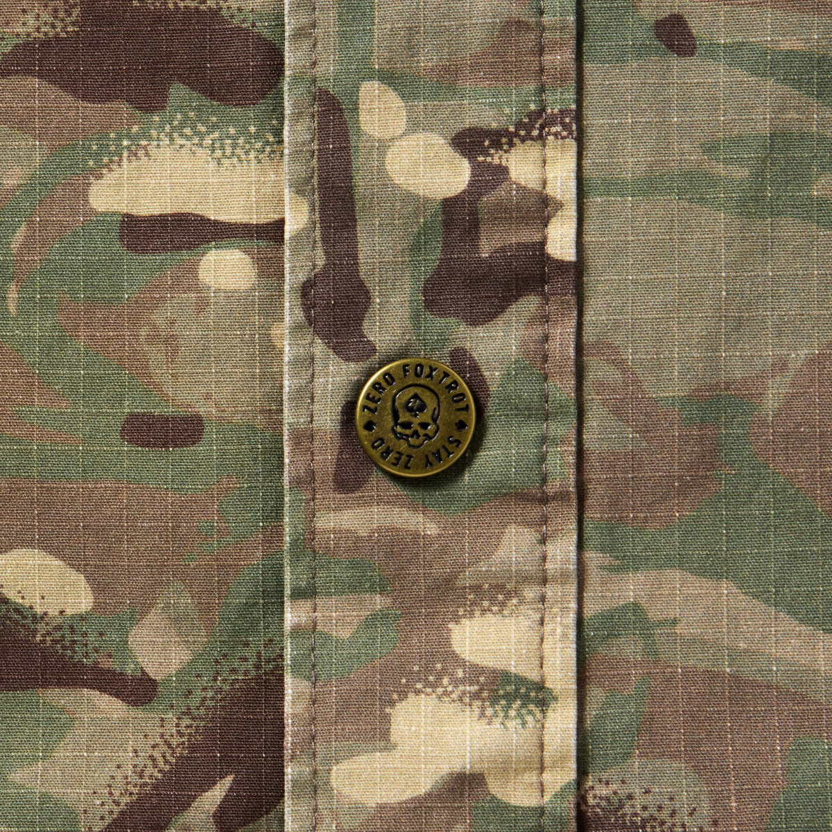 Close-up of camouflage fabric with a metal button featuring a skull design on the Chore Jacket.