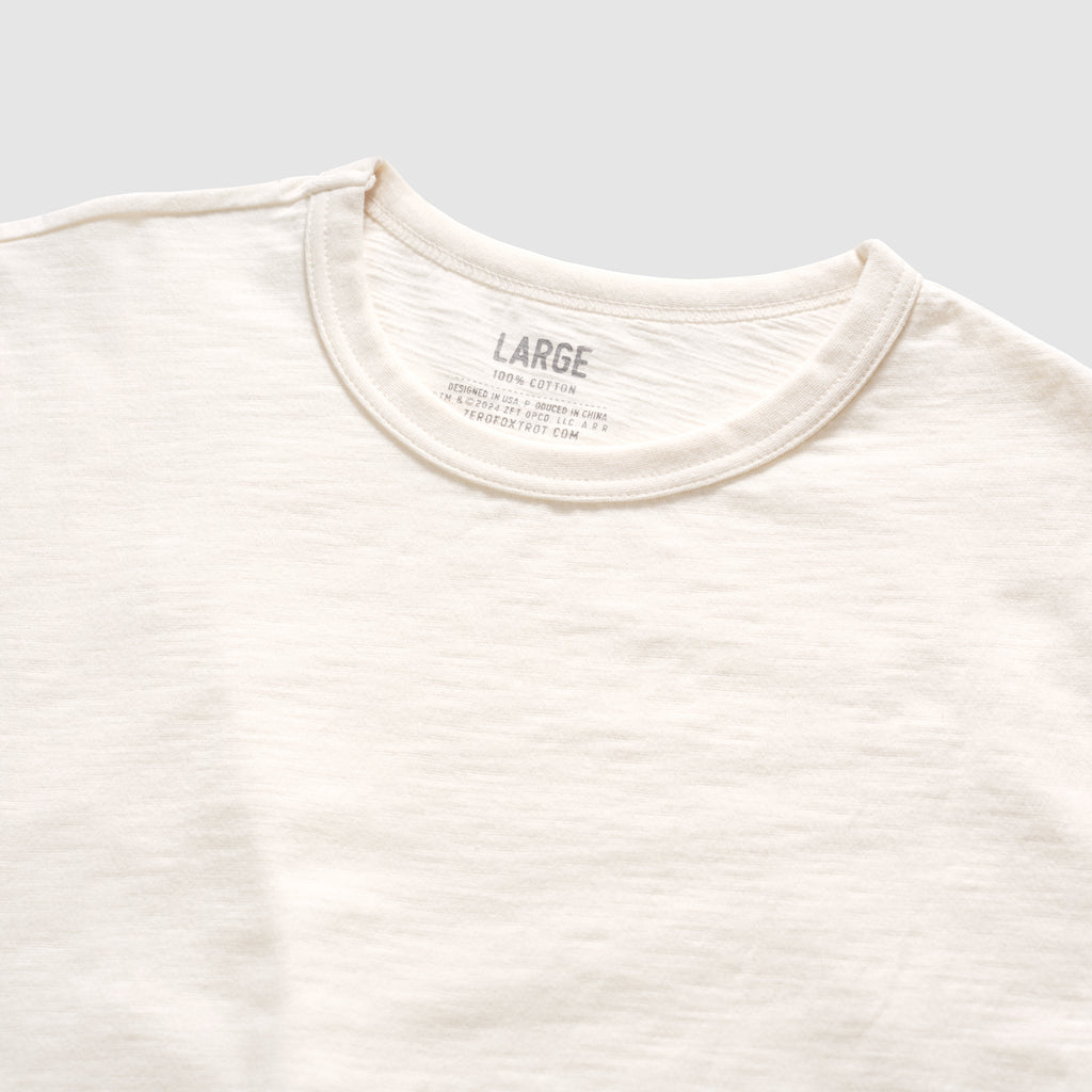 Close-up view of a light bone-colored Cotton Skivvy Tee featuring a round neckline and soft, textured cotton fabric in size large.
