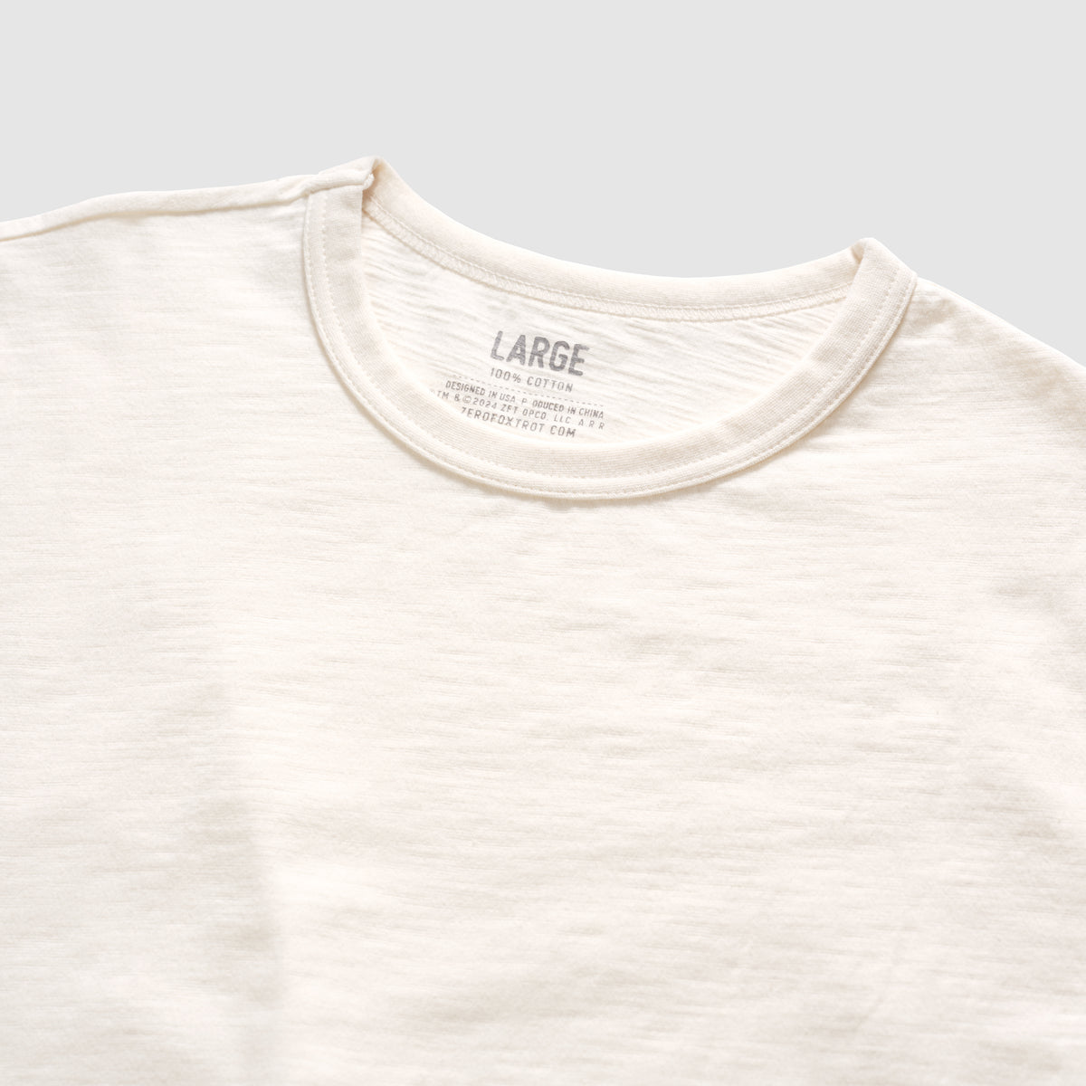 Close-up view of a light bone-colored Cotton Skivvy Tee featuring a round neckline and soft, textured cotton fabric in size large.