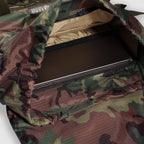 Woobie Backpack with a woodland camouflage pattern shown open, revealing a padded compartment holding a laptop inside the main storage area.