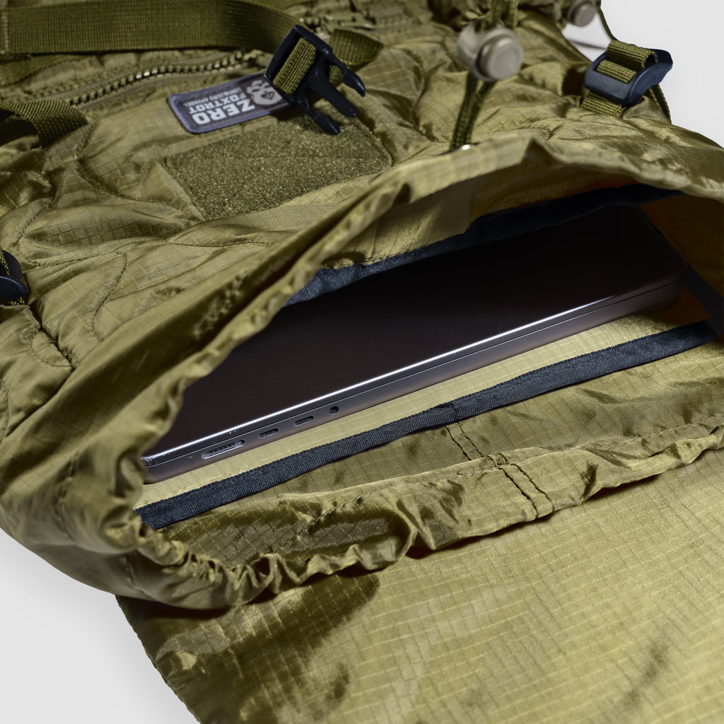 Woobie Backpack in olive green shown open with a laptop partially inserted inside the padded interior compartment.