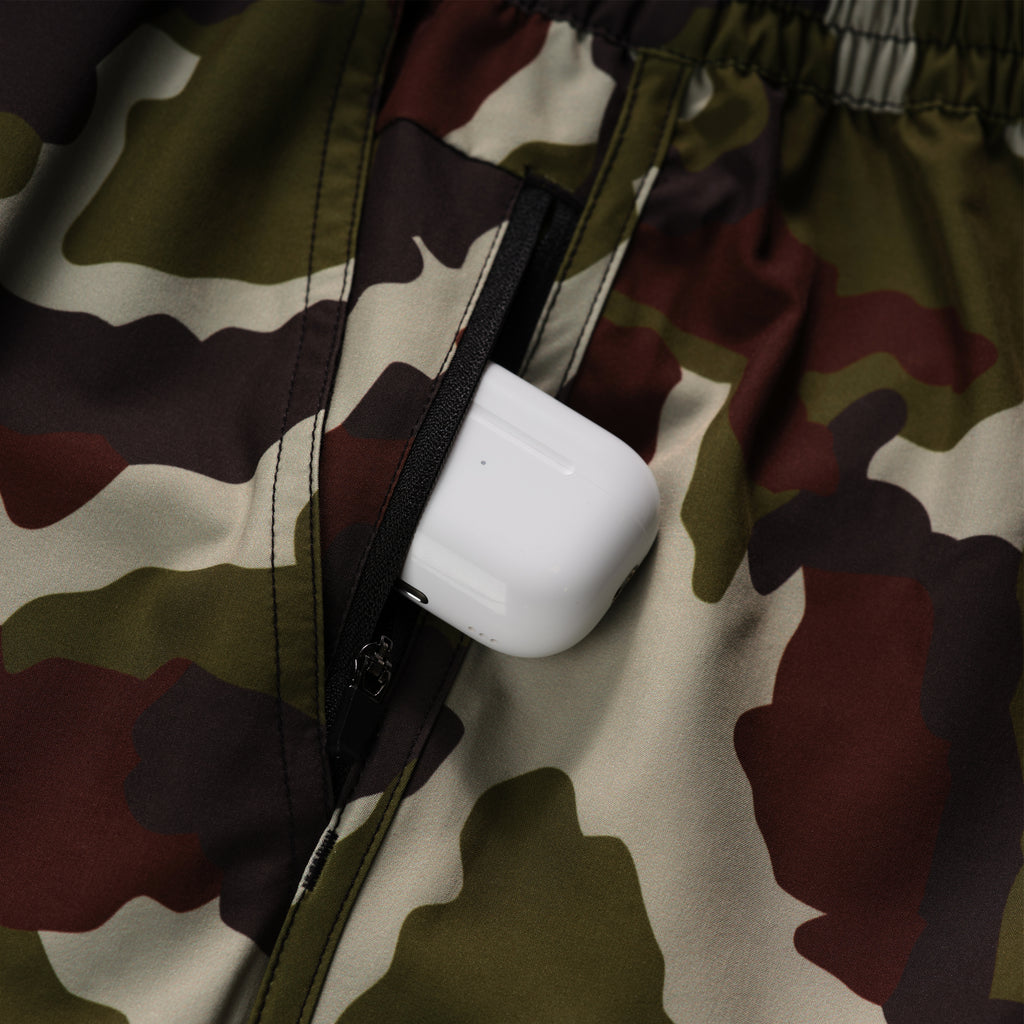 Close-up of a camouflage fabric pocket with a white wireless earbud case partially inside, showcasing the zipper detail on the Zero Shorts - 7" Inseam.