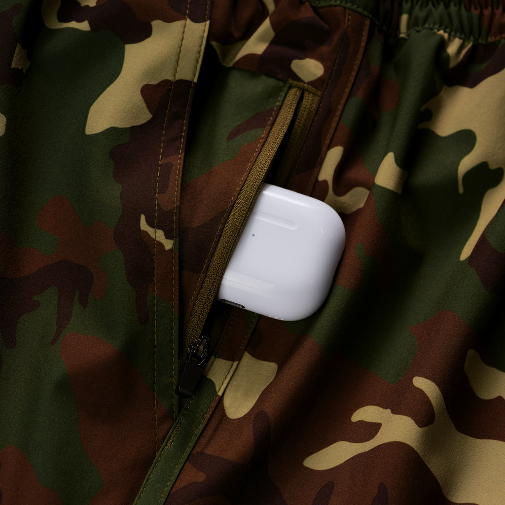 Close-up of a camo-patterned pocket with a zipper partially open, holding a white wireless earbud case, highlighting functionality of the Zero Shorts - 9" Inseam.