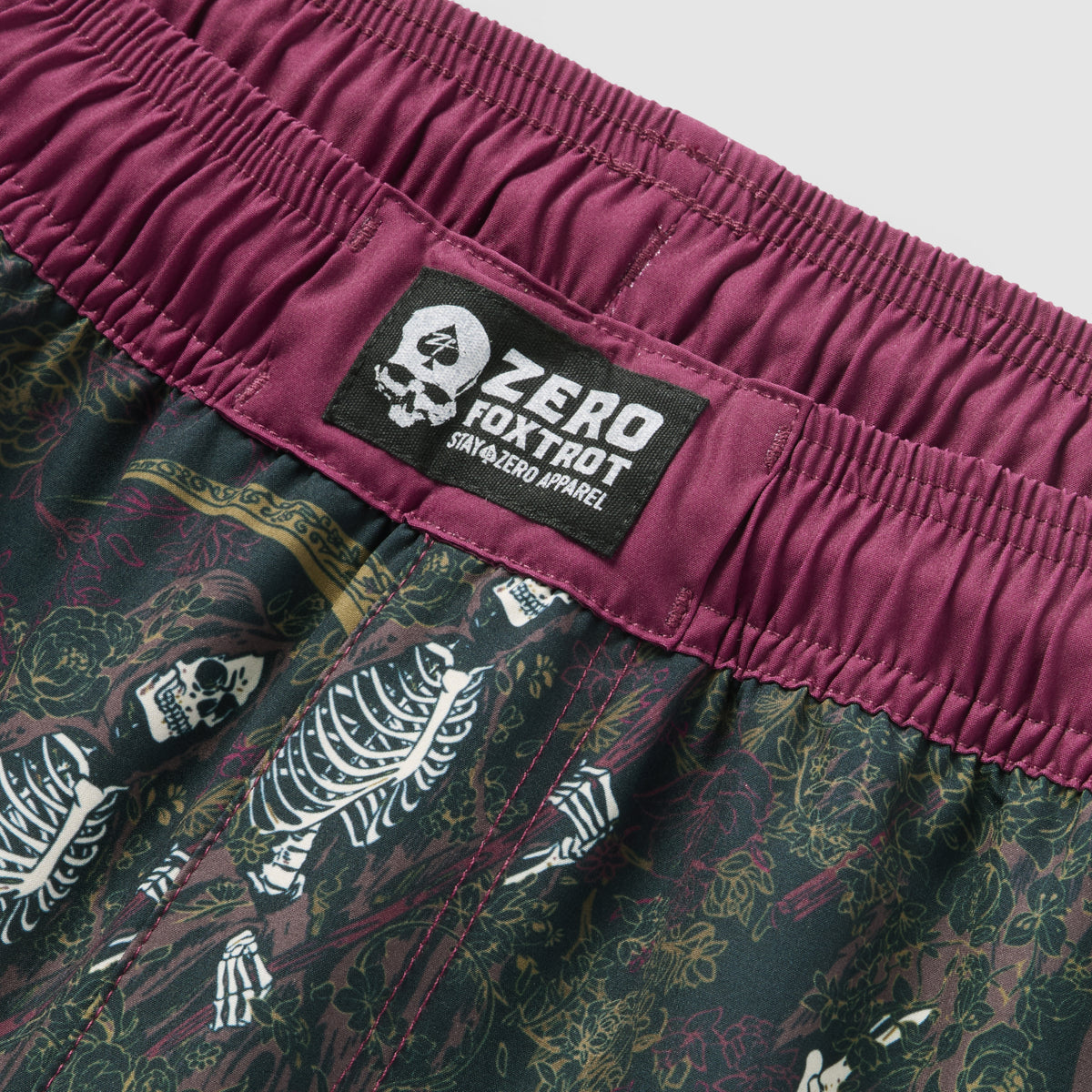 Close-up of the waistband area of ZF Fight Shorts featuring a maroon elastic waistband with a black and white patch logo, and a detailed skeleton and floral pattern on the fabric below.